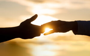 Image of two hands touching with a sunset in the background. This image represents the support that people can receive when using anxiety treatment in Baltimore, MD to heal from racial injustice. | 21286 | 21093