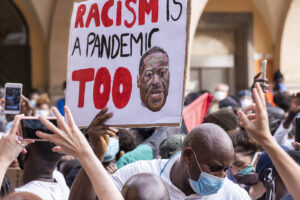 Image of a protest with a sign reading "racism is a pandemic too" being help up in the center. This image illustrates the need for anxiety treatment in Baltimore, MD to aid in healing due racial injustice. | 21209 | 21204