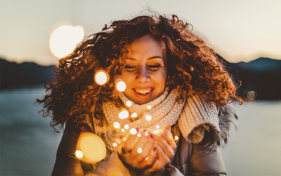 Woman holding festive lights and smiling, representing how we can set and keep our new year's resolutions if we know what makes them fail.