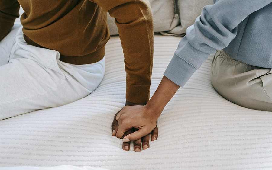 Black couple holding hands on bed, representing how the support of a partner can be crucial to help a loved one with depression.