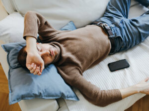 Photo of a tired man laying on the couch. This represents how depression can make you feel tired and fatigued and the importance of recognizing these sigs to seek help from a therapist.
