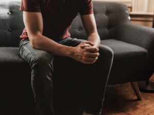 Photo of a man sitting in the couch, thinking, with his hands crossed. This represents someone thinking about seeking treatment for depression.