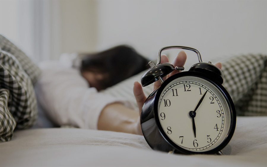 Woman in bed turning off the alarm clock. This represents how depression and daylight savings time can affect your mood and energy levels.