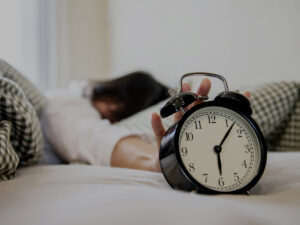 Photo of a woman in bed turning off the alarm clock. This represents how depression and daylight savings time can affect your mood and energy levels.