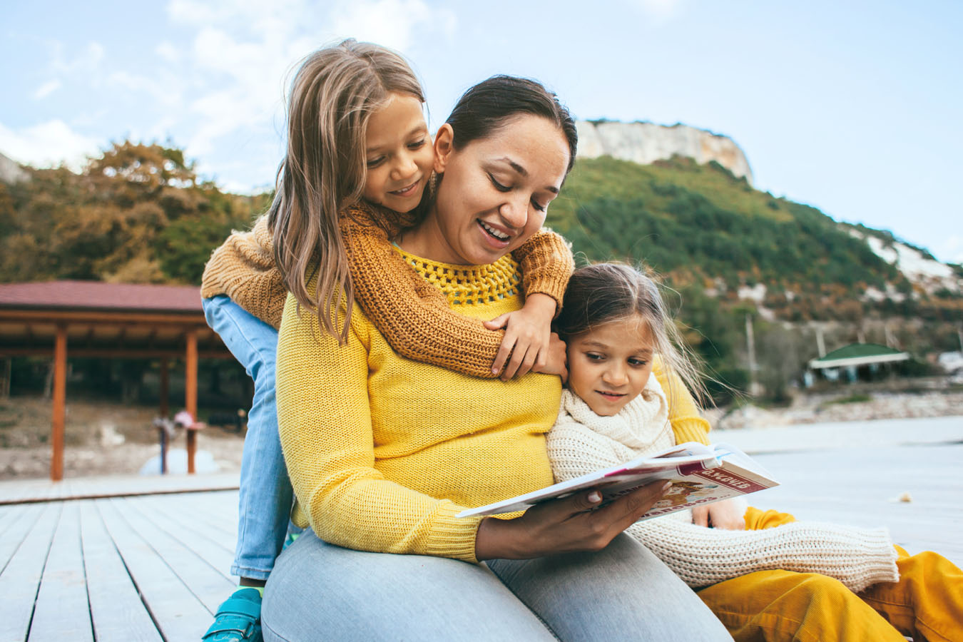 Young mother and two daughters reading a book outdoors | Therapy for women in Baltimore, MD with a women's therapist | Counseling for women | New Connections Counseling Center | Baltimore, MD" width="300" height="200"