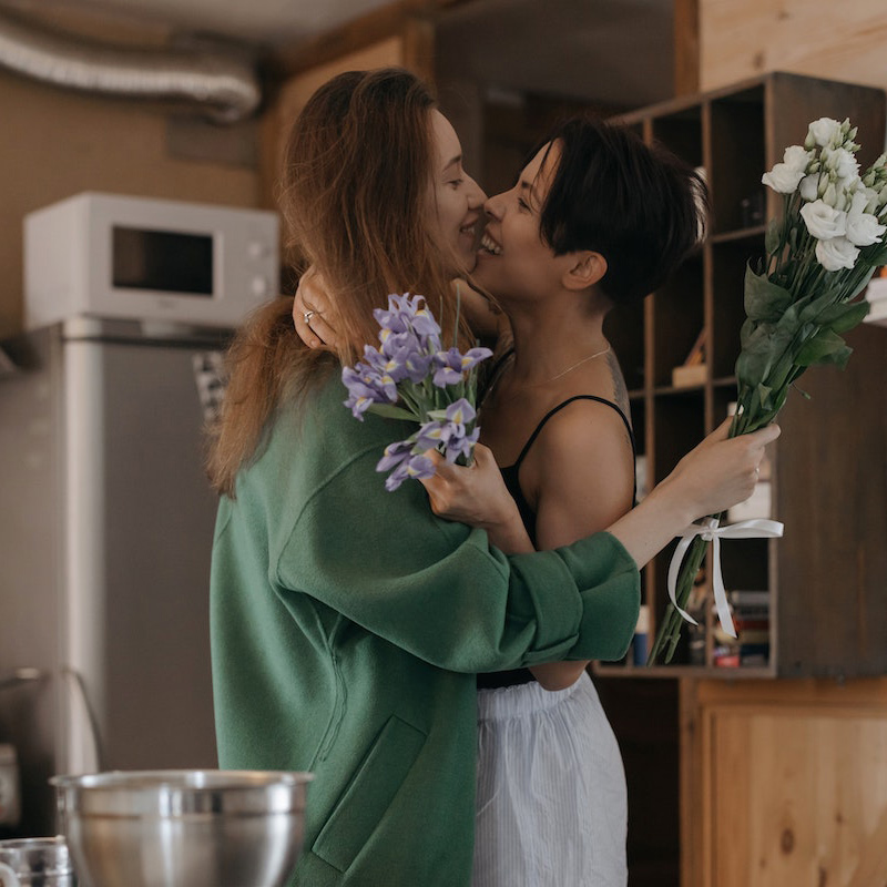 Image of a female/female couple hugging and smiling in their kitchen. Working through marriage counseling in Baltimore, MD can help couples discover their love for one another again. | 21286 | 21093" width="359" height="239