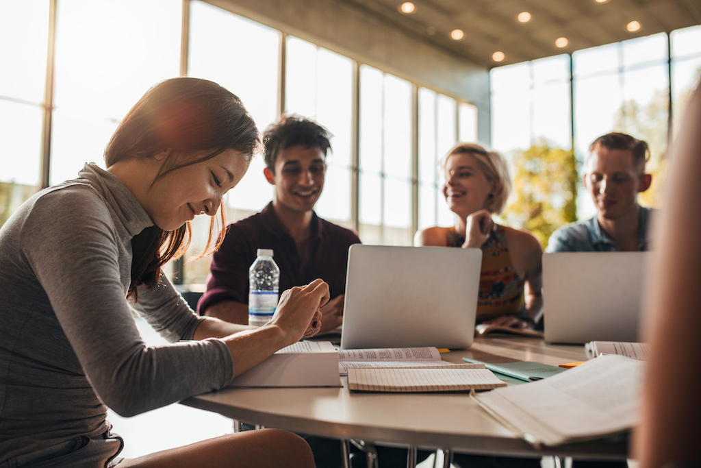 group of college students sitting at a table working on homework on computers. Help making friends is a common concern discussed in therapy for college students at New Connections Counseling Center in Baltimore, MD 21210" width="300" height="200"