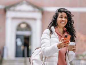 Photo of a college student happily texting her friends after arriving to campus. This represents how coping with with depression in college and being aware of the symptoms can help you have a positive and fulfilling college experience.