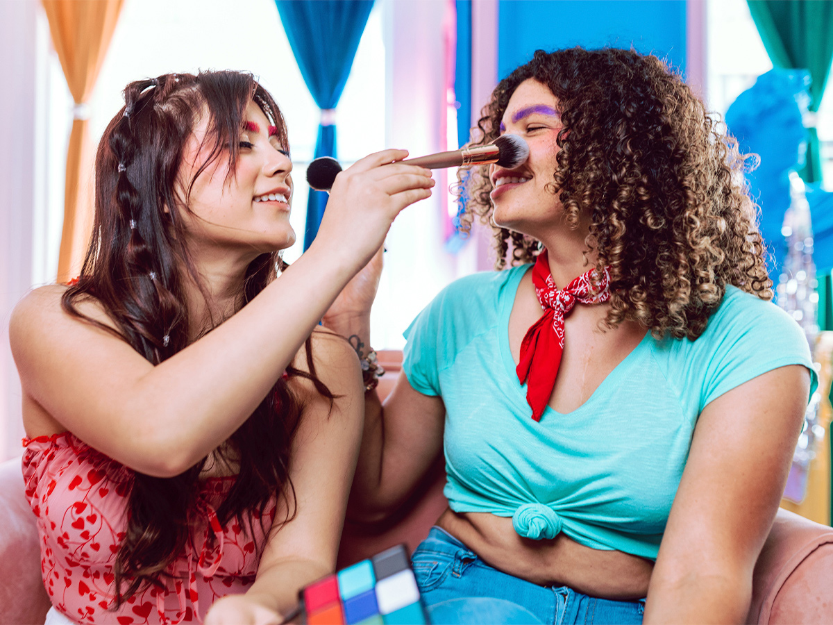 Two gender-nonconforming individuals doing each other makeup and smiling. This represents two people on the Baltimore area that are aware and informed about gender affirmation care." width="319" height="239"