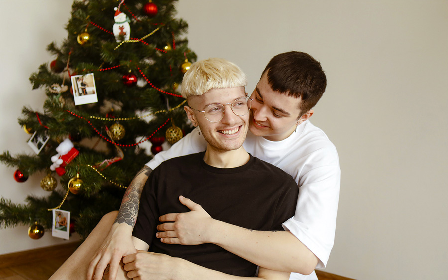 Queer couple hugging happily and celebrating the holiday season together. This represents how it is important to focus on your own self-care and self-acceptance to help you navigate the holidays when LGBTQ+.