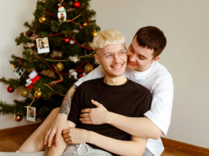 Photo of a gay couple hugging happily and celebrating the holiday season together. This represents how it is important to focus on your own self-care and self-acceptance to help you navigate the holidays when LGBTQ+.