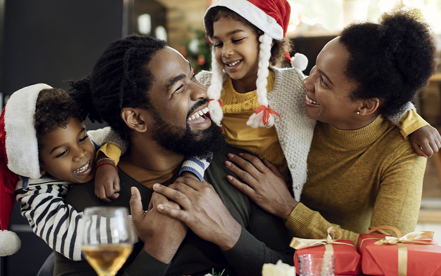 BIPOC family happily celebrating Christmas together. This represents how taking steps to cope with holiday stress and anxiety will allow you to enjoy yourself during the holidays.