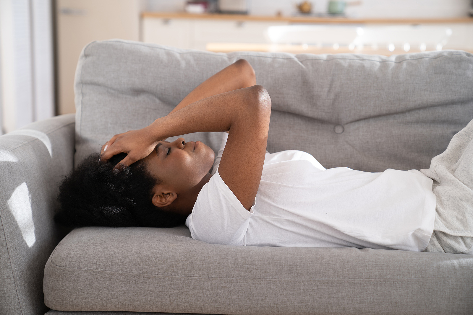Image of a young woman sitting on a couch with her hands held to her forehead. The woman in this image depicts what someone struggling with symptoms of PTSD may look like. Someone with PTSD could seek help from a trauma therapist in Baltimore, MD. 21286 | 21093