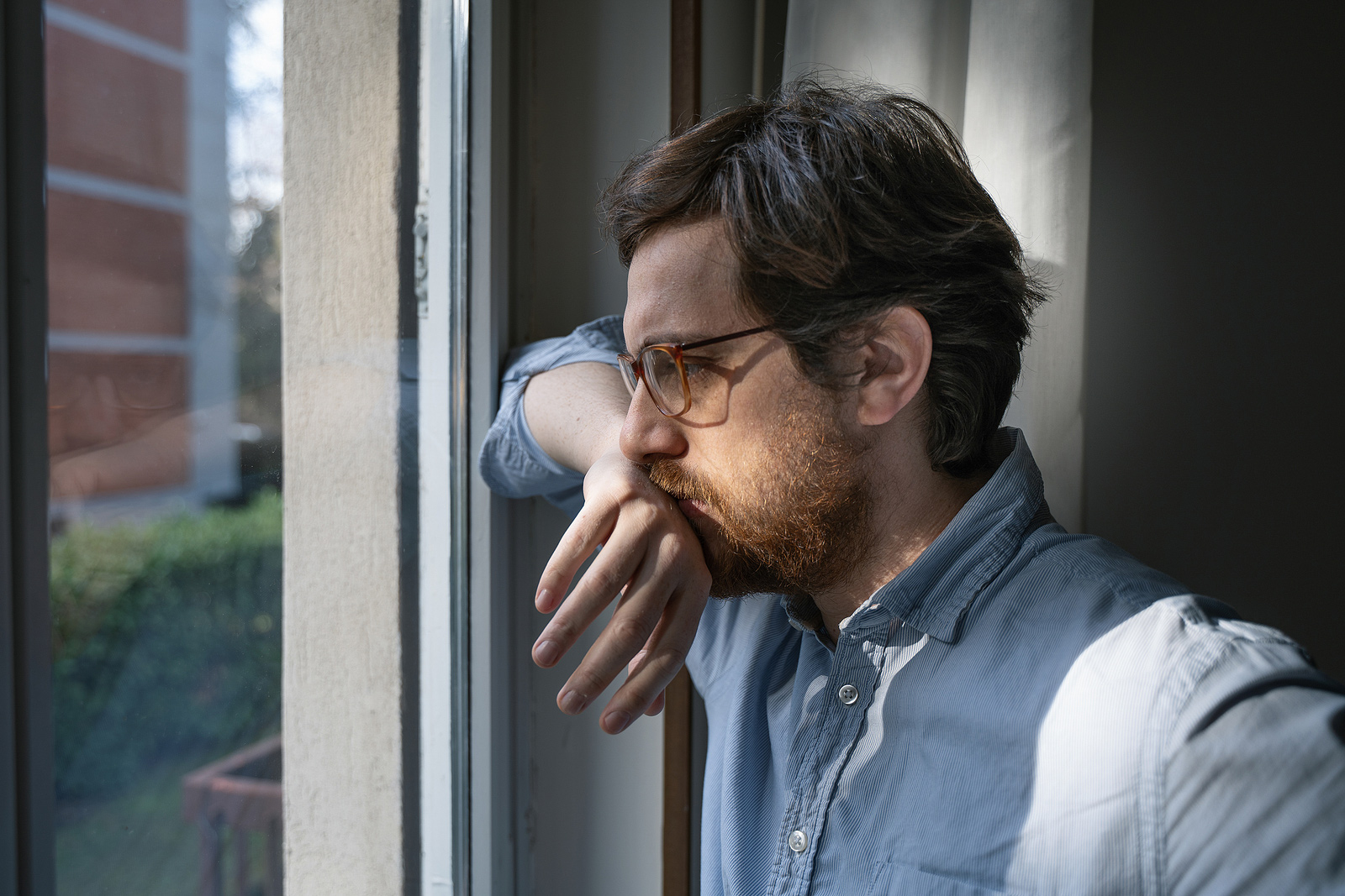 Image of a man looking out the window with his hand on his mouth. He represents what someone experiencing trauma symptoms may look like. Those searching "EDMR therapy near me" can find support from an EMDR therapist in Baltimore, MD. 21210 | 21212