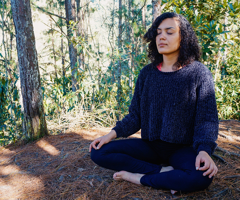 Image of a woman sitting in the forest with her eyes closed meditating. She represents the peace you can find from working with an EMDR therapist in Baltimore, MD to treat trauma symptoms. | 21286 | 21093