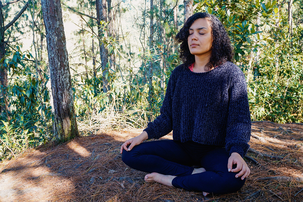 Image of a woman sitting in the forest with her eyes closed meditating. She represents the peace you can find from working with an EMDR therapist in Baltimore, MD to treat trauma symptoms. | 21286 | 21093
