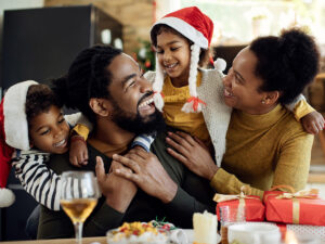Photo of a BIPOC family happily celebrating Christmas together. This represents how taking steps to cope with holiday stress and anxiety will allow you to enjoy yourself during the holidays.