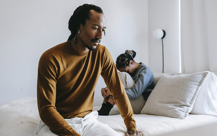 BIPOC couple sitting on the bed with their backs turned on each other, representing how understanding infidelity and how to stop cheating can be crucial for moving forward in a relationship.