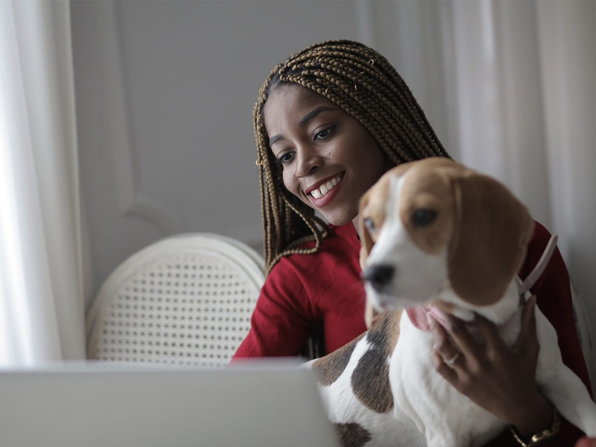 Photo of a BIPOC woman sitting in front of a laptop with her dog on her lap. This represents how you can get the support you need from the comfort of your own home and even with your furry friend beside you.
