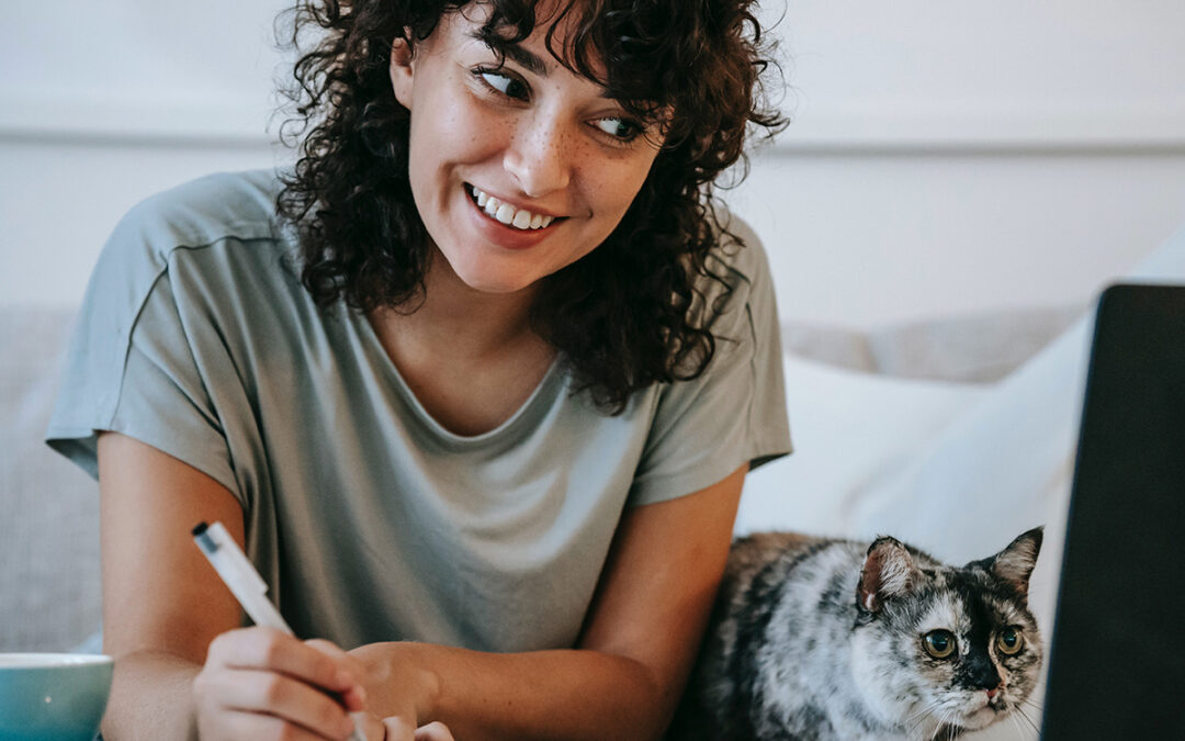 Photo of a young adult woman connected on her laptop to a therapy session from her home, in the company of her cat. This represents how choosing online therapy in Baltimore has many benefits.