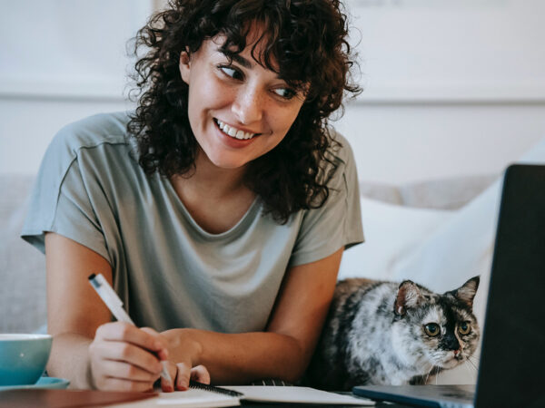 Photo of a young adult woman connected on her laptop to a therapy session from her home, in the company of her cat. This represents how choosing online therapy in Baltimore has many benefits.