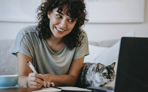 Young adult woman connected on her laptop to a therapy session from her home, in the company of her cat. This represents how choosing online therapy in Baltimore has many benefits.