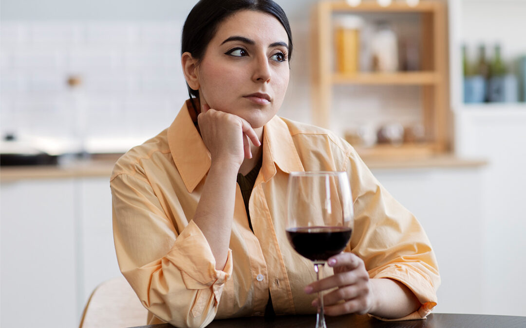 Photo of a woman drinking a glass of wine alone, with an introspective and worried look. This represents that while some people tend to drink to relax and alleviate anxiety, alcohol can actually cause anxiety or worsen it.