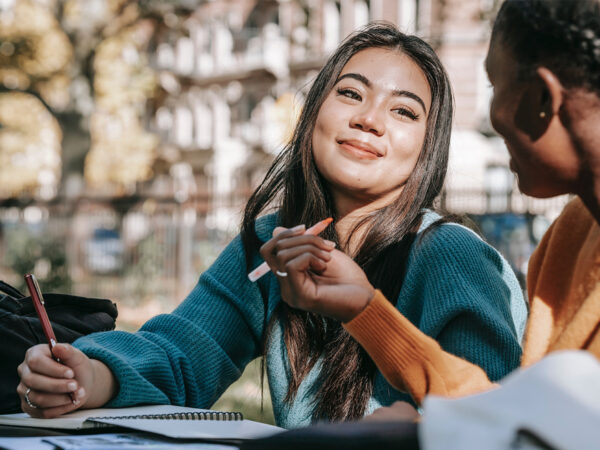 Photo of a student smiling and having a good time while studying with a friend at college. This represents how parents' support of their college students' success is crucial to help their kids transition and achieve a fulfilling and positive college experience.