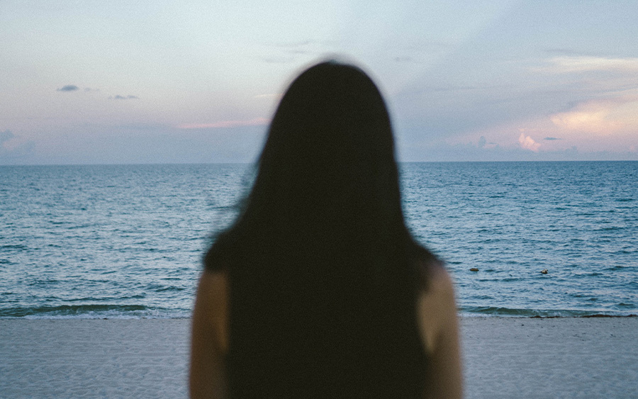 Photo of a woman dressed in black looking at the sea at dawn, with her back facing the camera. This represents how we can reflect on what the movie Titanic can teach us about grief and moving on while holding on to the love we lost.