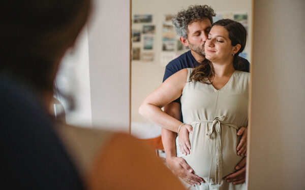 Photo of a couple holding each other in front of a mirror, where both of them have their hands resting on the pregnant woman's belly. This represents how therapy can help you cope with the thought about "Why Are Major Life Changes So Stressful?".