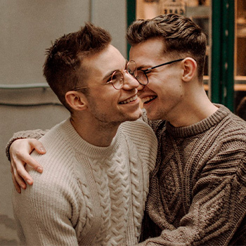 Photo of a queer couple holding each other and laughing together. This represents how LGBTQ therapy can help you connect with your identity and find happiness.