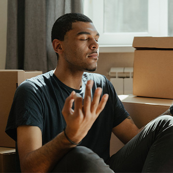 Photo of a man sitting on the floor of his new home surrounded by unpacked boxes trying to cope through meditation. This represents how counseling for life transitions can help you develop new skills to deal with big changes in your life.