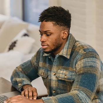 Photo of a man working on his computer with a concentrated expression. This represents how men's therapy can help you manage the challenges in your life.