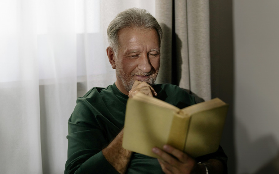 Photo of an older man reading a book and reminiscing about his own story. This represents how the experience of a traumatic loss marks a person's entire life journey.