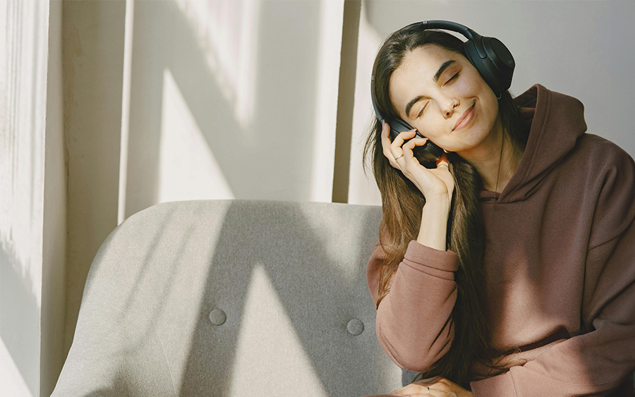 Photo of a woman with a relaxed and happy expression listening to music. This represents the benefits of music on our brain, mental health and overall well-being.