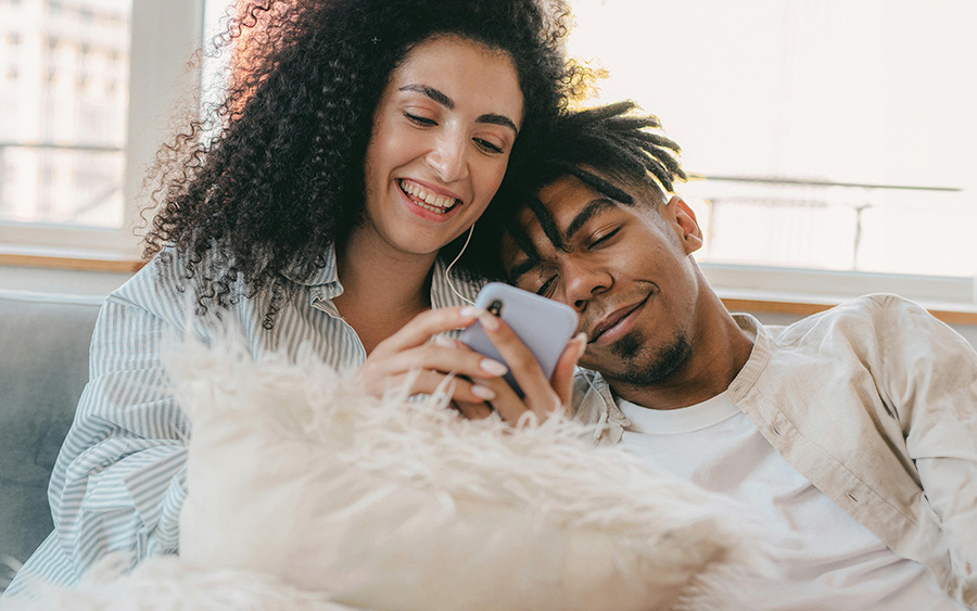 BIPOC couple with a happy and affectionate expression, watching something on the woman's phone. This represents how setting healthy relationship boundaries leads to balanced and happier bonds.