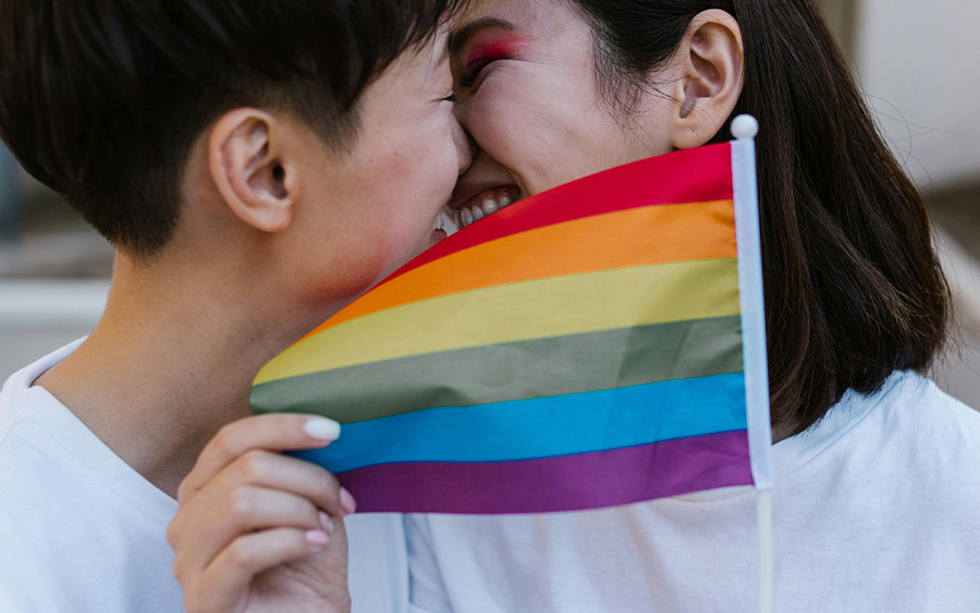 LGBTQ couple kissing and holding a pride flag. This represents how o celebrating Pride in Baltimore (& everywhere else) is a powerful way to come together for diversity, inclusion, and love.