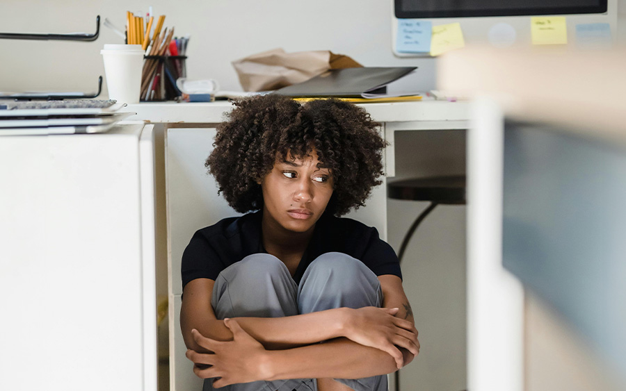 Woman huddled under her desk, worried about her work issues and how she could better support her mental health in the workplace.