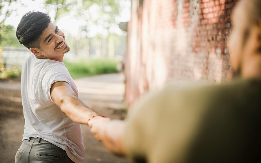 Man looking back and smiling to his parter while holding their hand, representing how couples can work together to overcome relationship insecurity and build a stronger, happier connection.