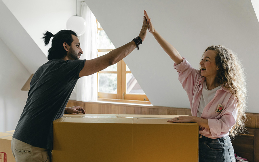 Happy couple high-fives while unboxing together in their new home, celebrating the progress they've made after working on their relationship goals through couples therapy.