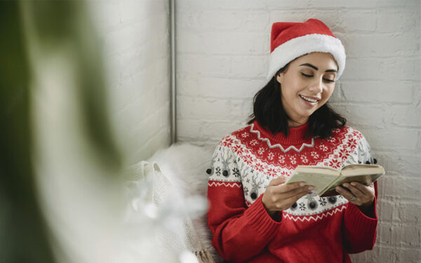 Young woman reading book on Christmas, representing how taking breaks is an effective way of dealing with stress during the holidays.