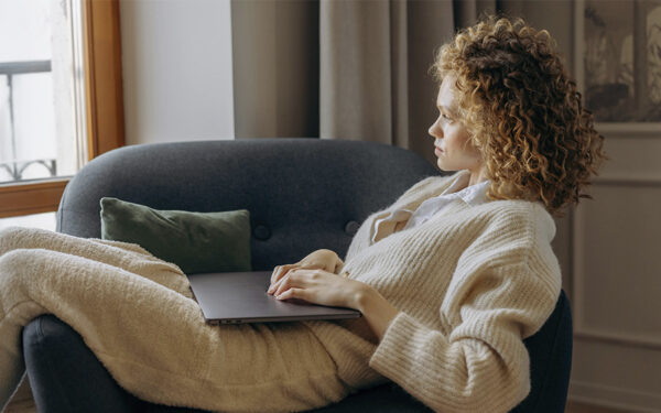 Woman sitting in a sofa chair with her laptop closed and looking pensive, represents how setting boundaries at work can protect us from burnout.