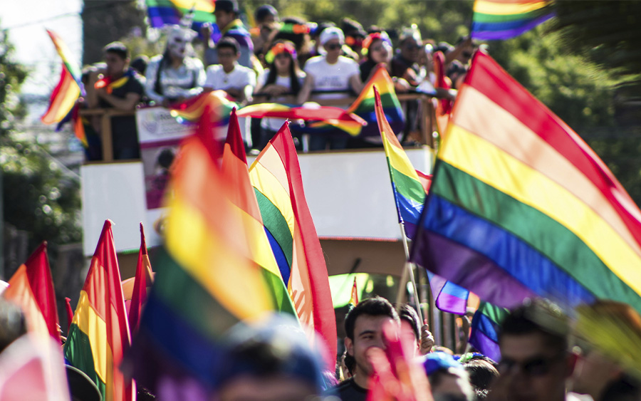 Pride parade with a crowd raising a lot of rainbow flags, represents why celebrating Pride this year matters more than ever.