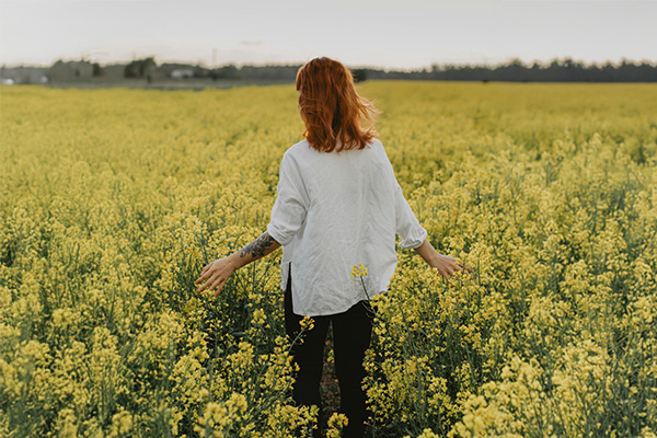 A person walking with their back turned in a field of yellow flowers represents how, with treatment, you can overcome anxiety and phobias.