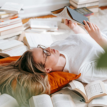 Woman reading while surrounded by piles of books, representing how ADHD treatment in Baltimore, MD can help you regain focus and control in your life.