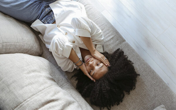 Woman lying on the couch with her hands on her face looking distressed, represents how DBT skills can help you strengthen your emotional regulation.