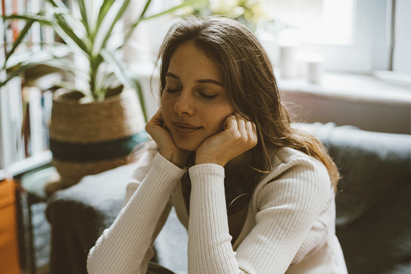 Woman sitting in a coach with her eyes closed and smiling, represents how EMDR can help you regain calm and reconnect with yourself.
